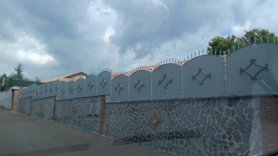 Un muro di pietra circondato da una recinzione metallica in una giornata nuvolosa.