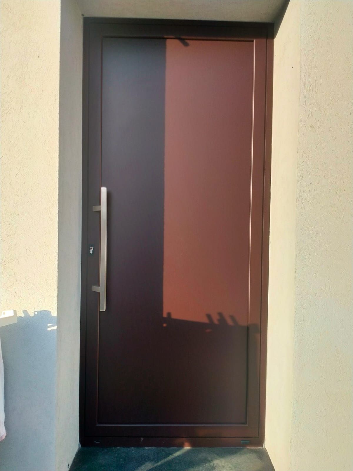 Una porta marrone con una maniglia in acciaio inossidabile si trova su una parete bianca.