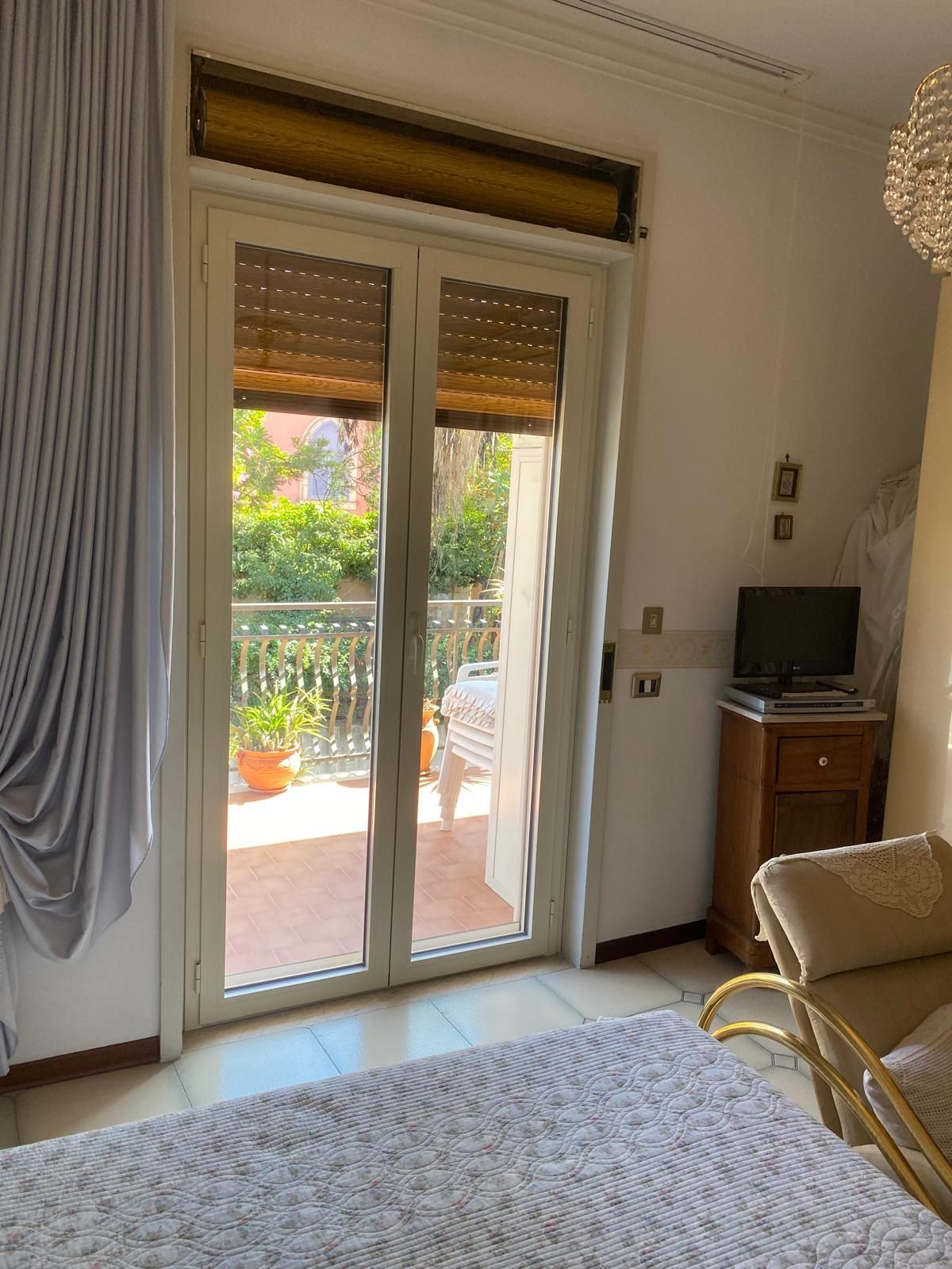 Una camera da letto con un letto, una sedia, una televisione e porte scorrevoli in vetro che conducono a un balcone.