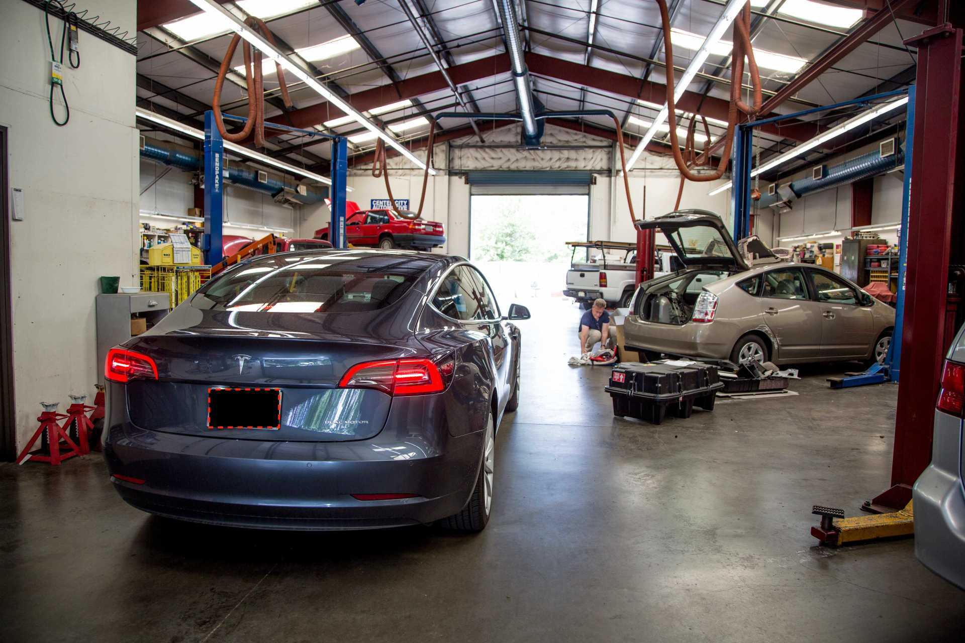 Tesla Model 3 in a repair shop with other vehicles.