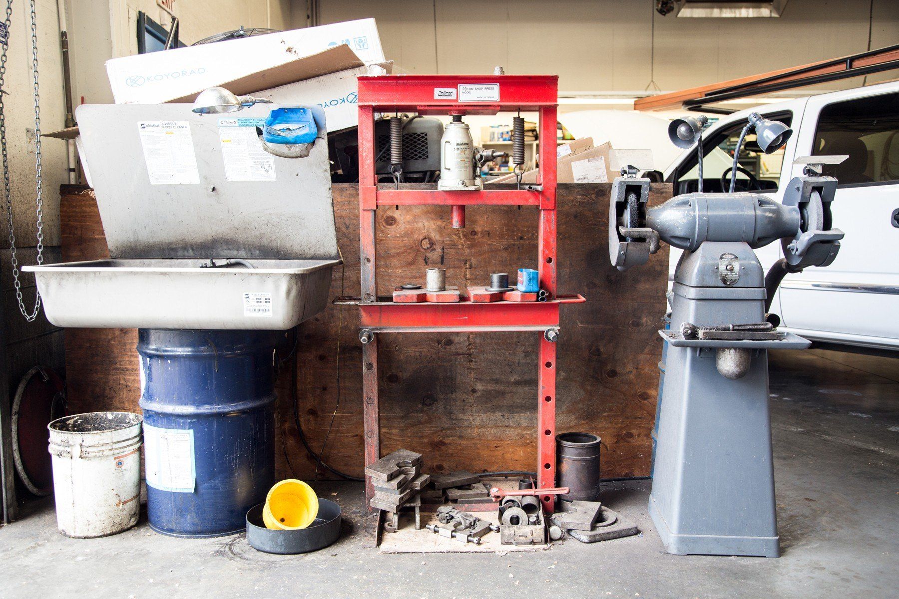 Workshop scene: Sink, red shelving unit with tools, grinder, and a white truck.