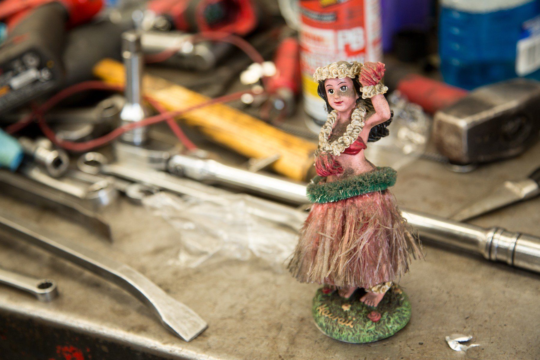 Hula girl figurine on a cluttered workbench with tools.