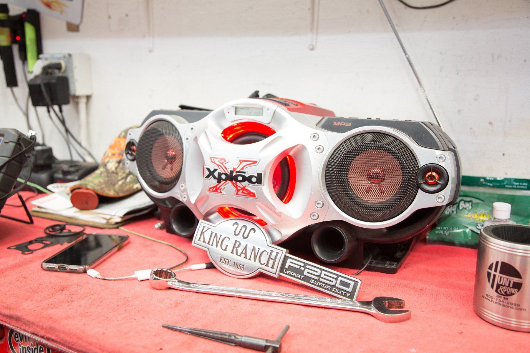 Xplod boombox on a red table with a King Ranch wrench. A phone and mug are also on the table.