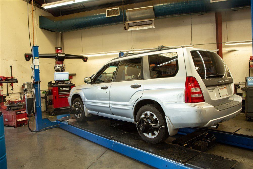 Silver SUV on a lift in a car repair shop, undergoing wheel alignment.