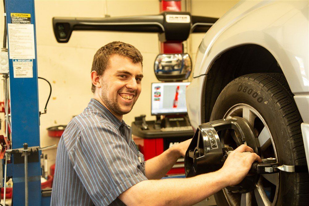 Mechanic smiling while adjusting a car wheel for alignment in a shop.