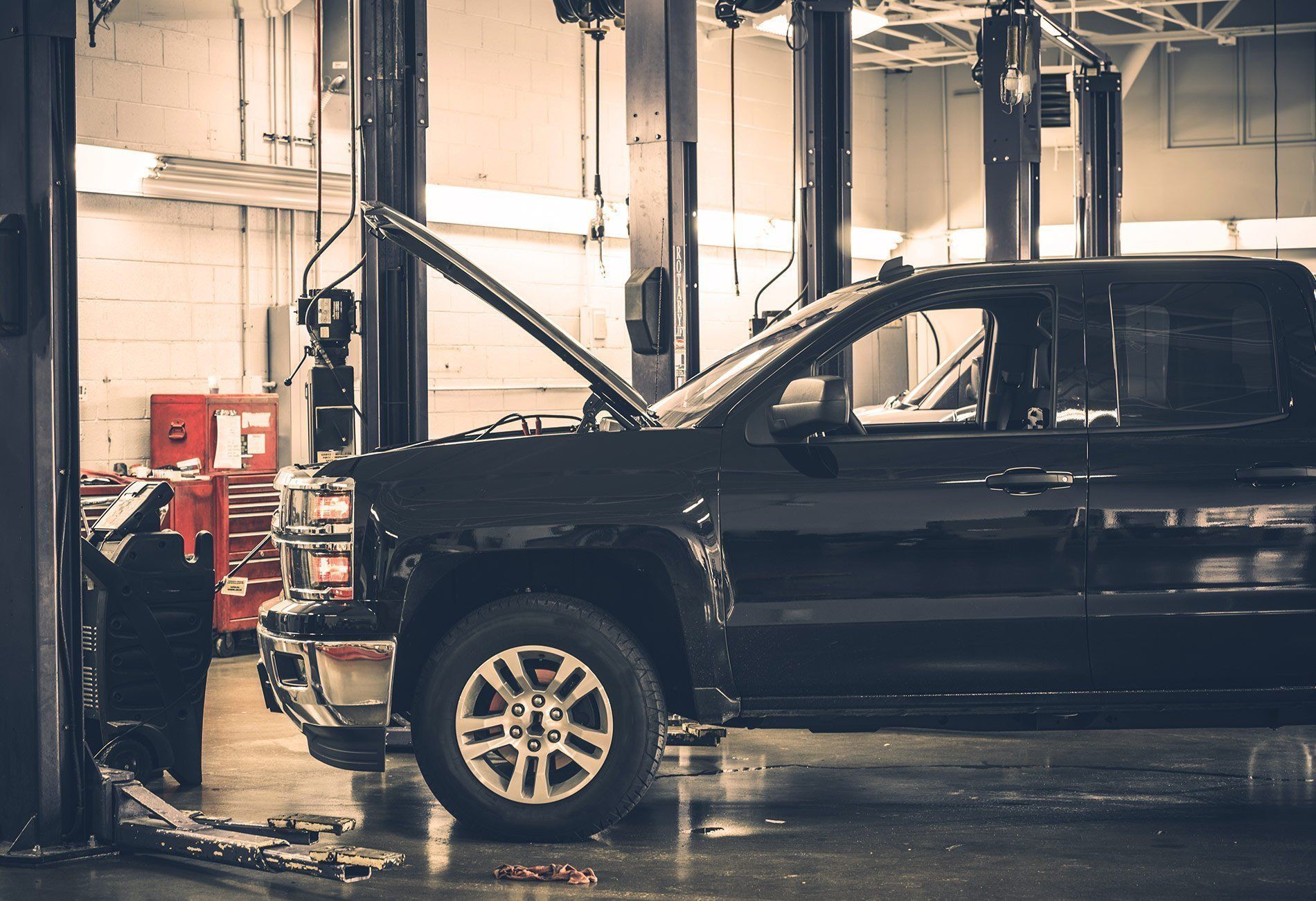 Black pickup truck with hood open in a car repair shop, under a lift.