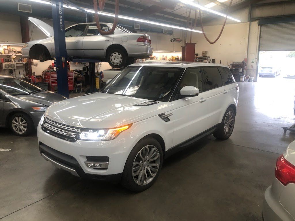 White Range Rover SUV parked in an auto repair shop with other cars.