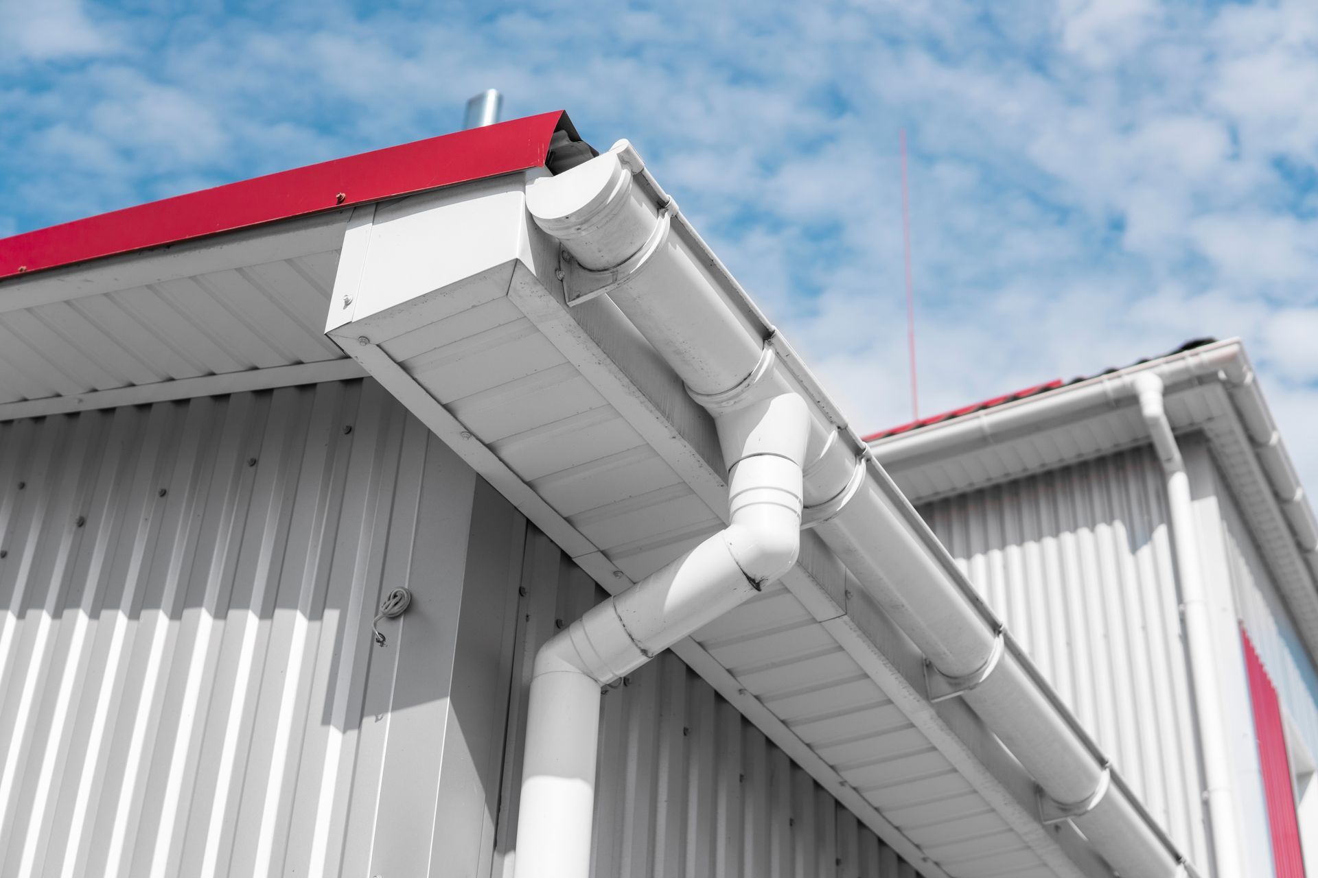 A white gutter on the side of a building with a red roof.