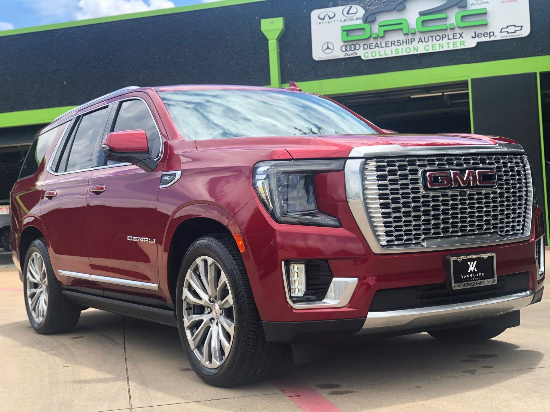 Red GMC Yukon Denali SUV parked in front of a collision center with green accents. The vehicle is shiny and new.