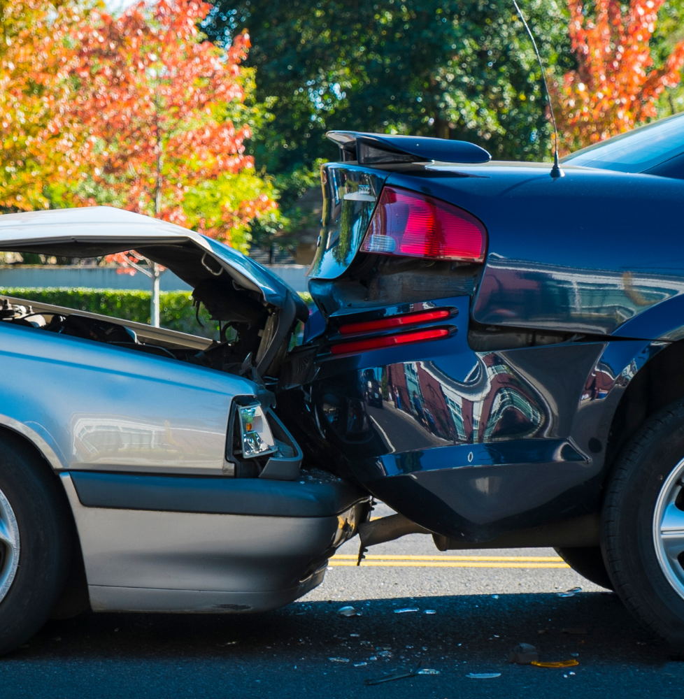 Two cars, silver and black, after a collision. The silver car's hood is up, the black car's rear is damaged.