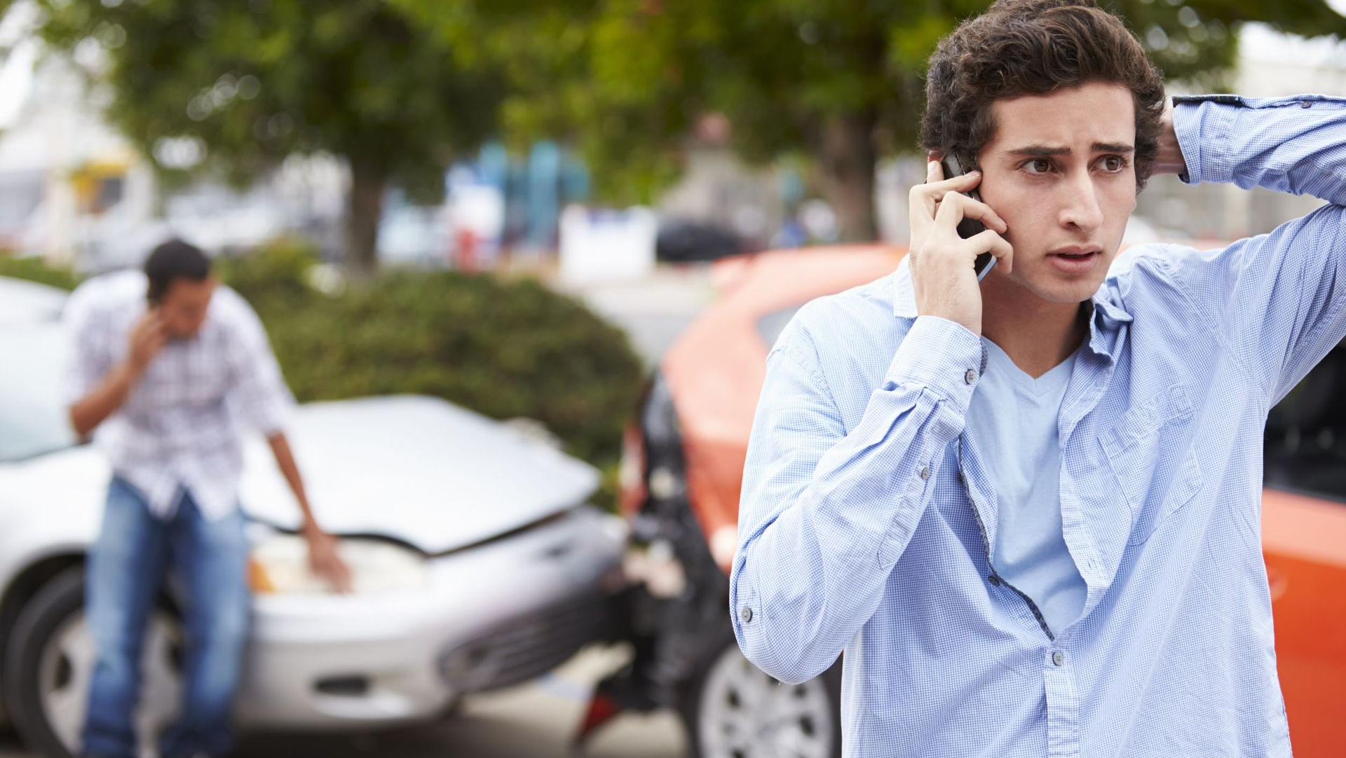 Two cars damaged in accident; man on phone looking concerned, another man nearby.