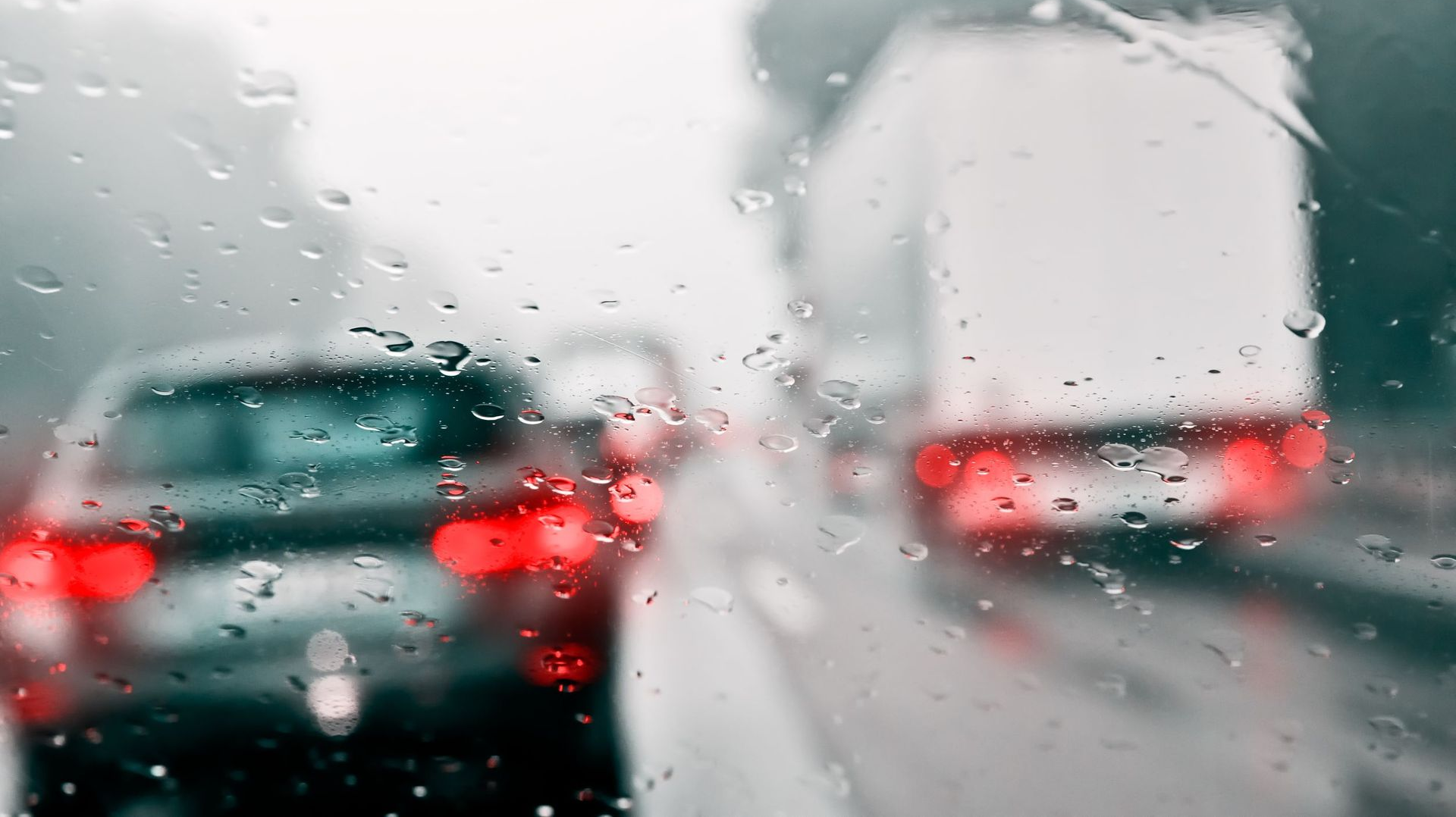 Rainy highway scene with blurred vehicles, including a car and a truck, visible through a wet windshield.