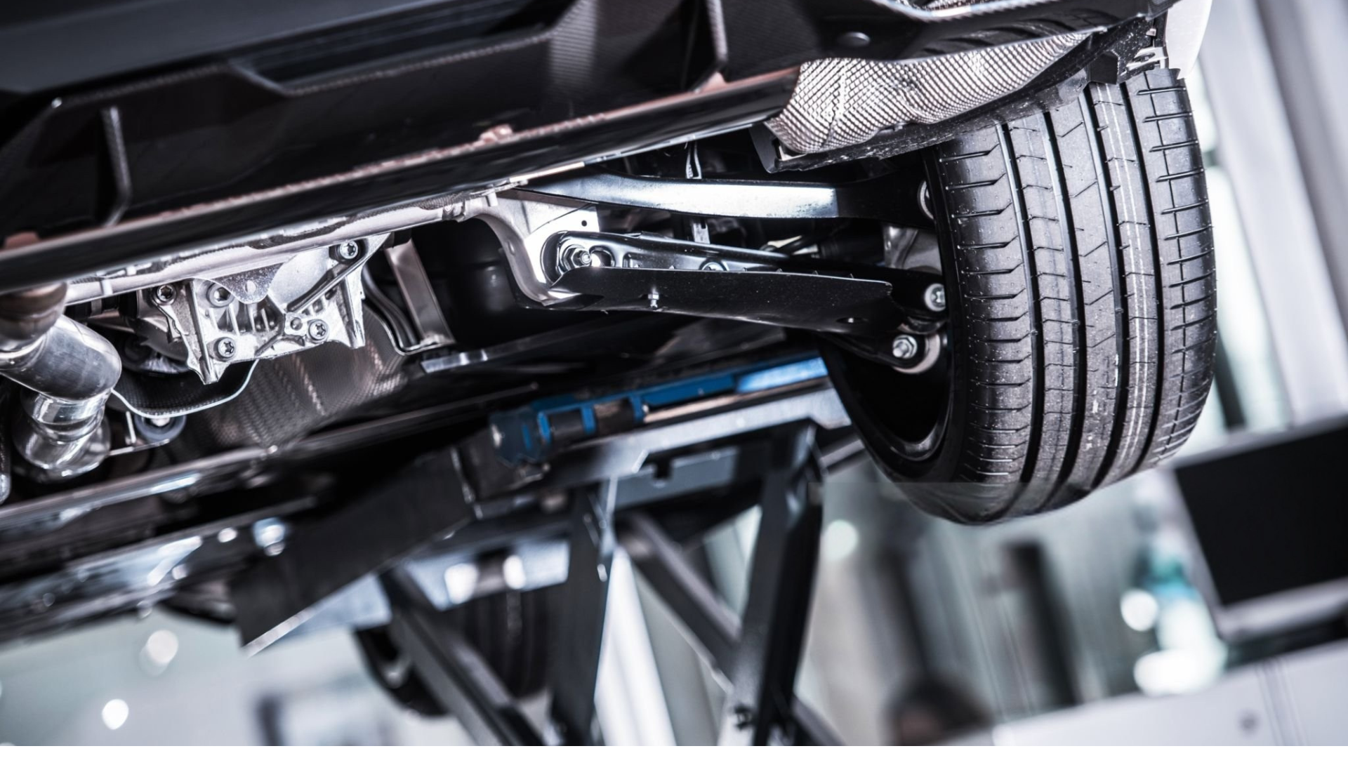 Undercarriage of a vehicle raised on a lift, showing the tire, suspension, exhaust, and other components.