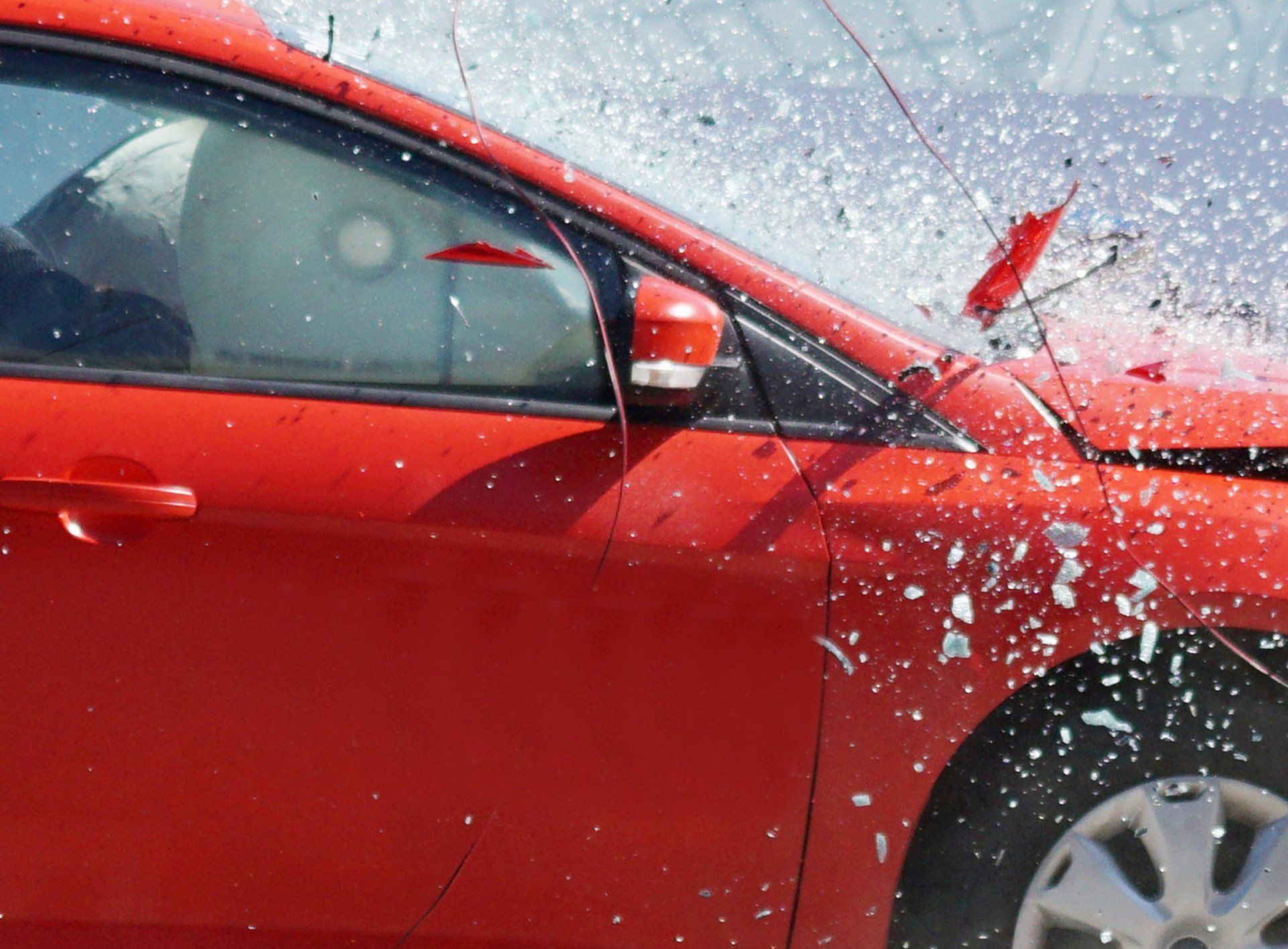 Red car with shattered windshield and visible damage, indicating a car accident.
