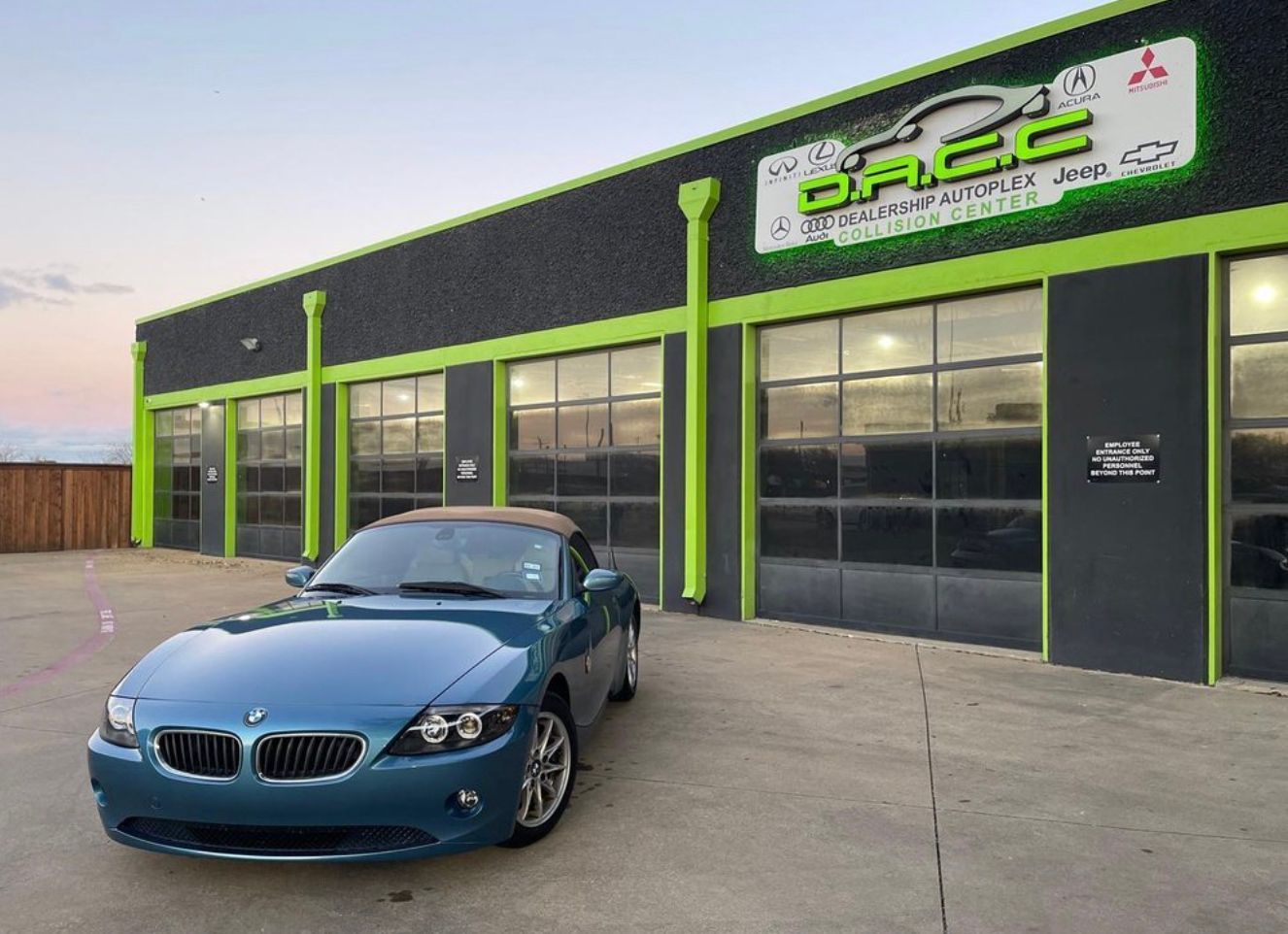 Blue BMW convertible parked in front of a green and black auto repair shop, 