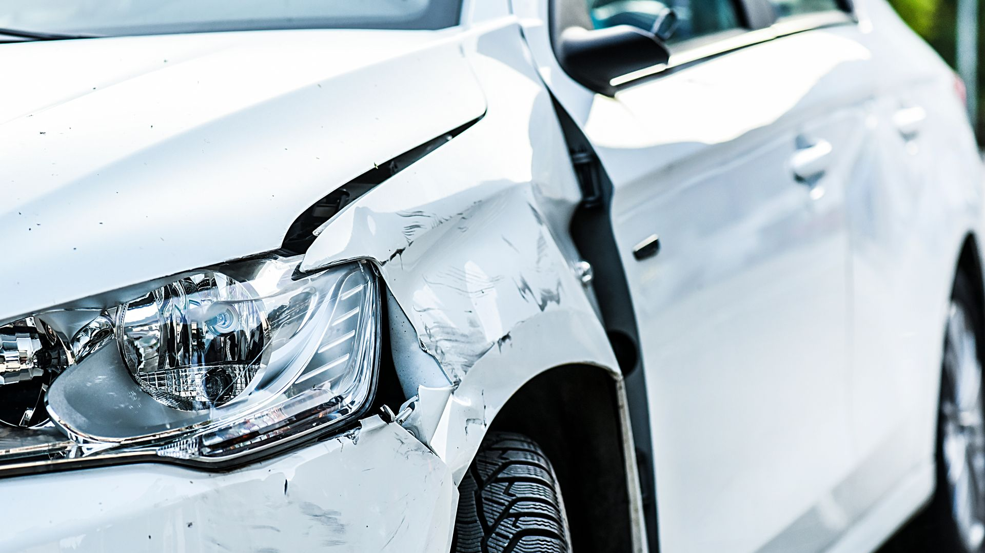 White car with damage to front left fender, headlight visible.