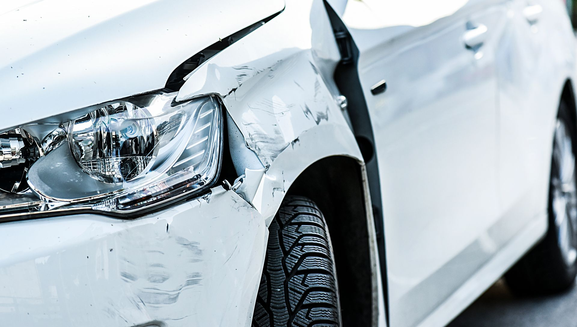White car with front-end damage, crumpled fender and broken headlight.