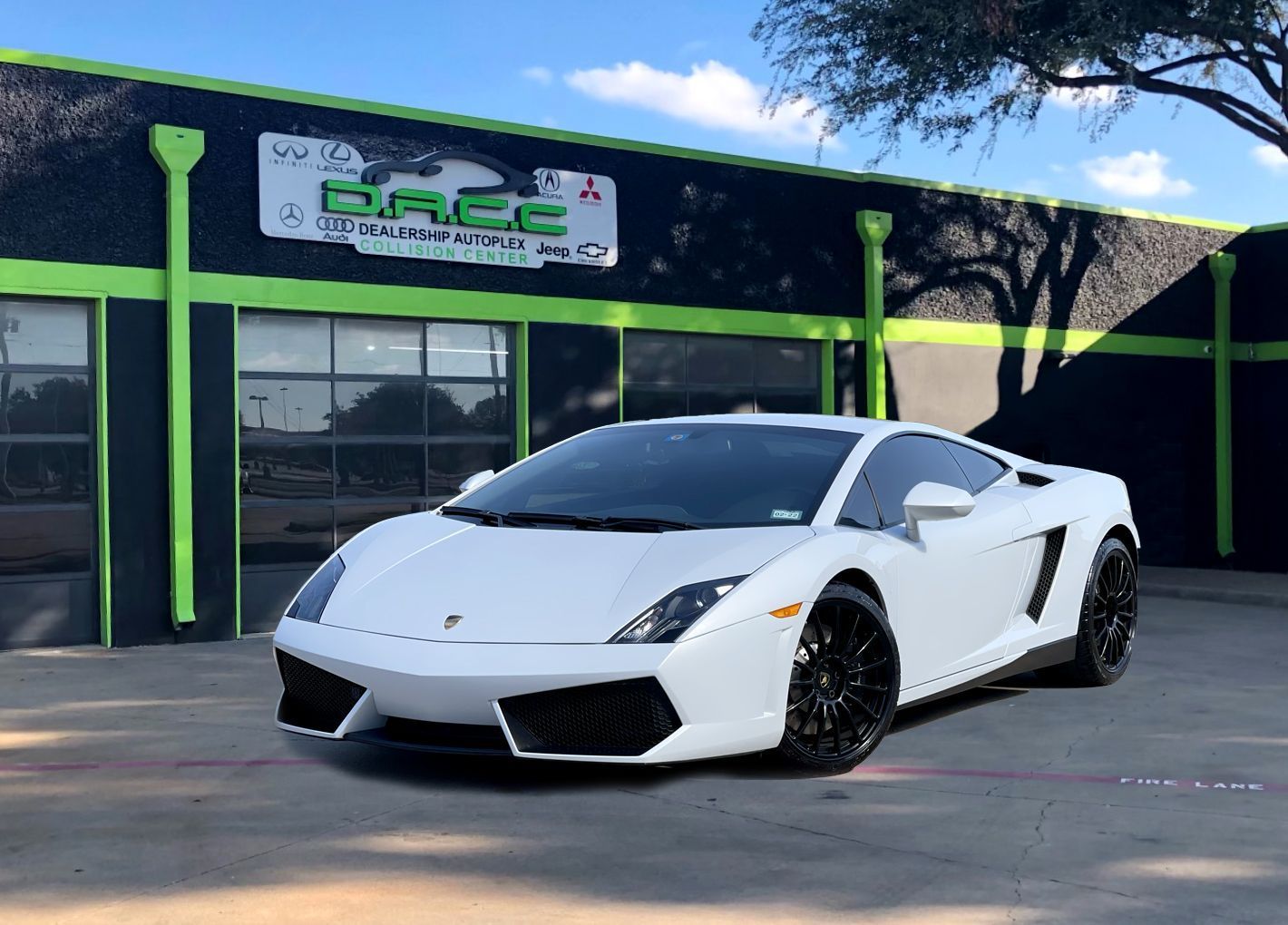 White Lamborghini parked in front of a car dealership with green and black accents.