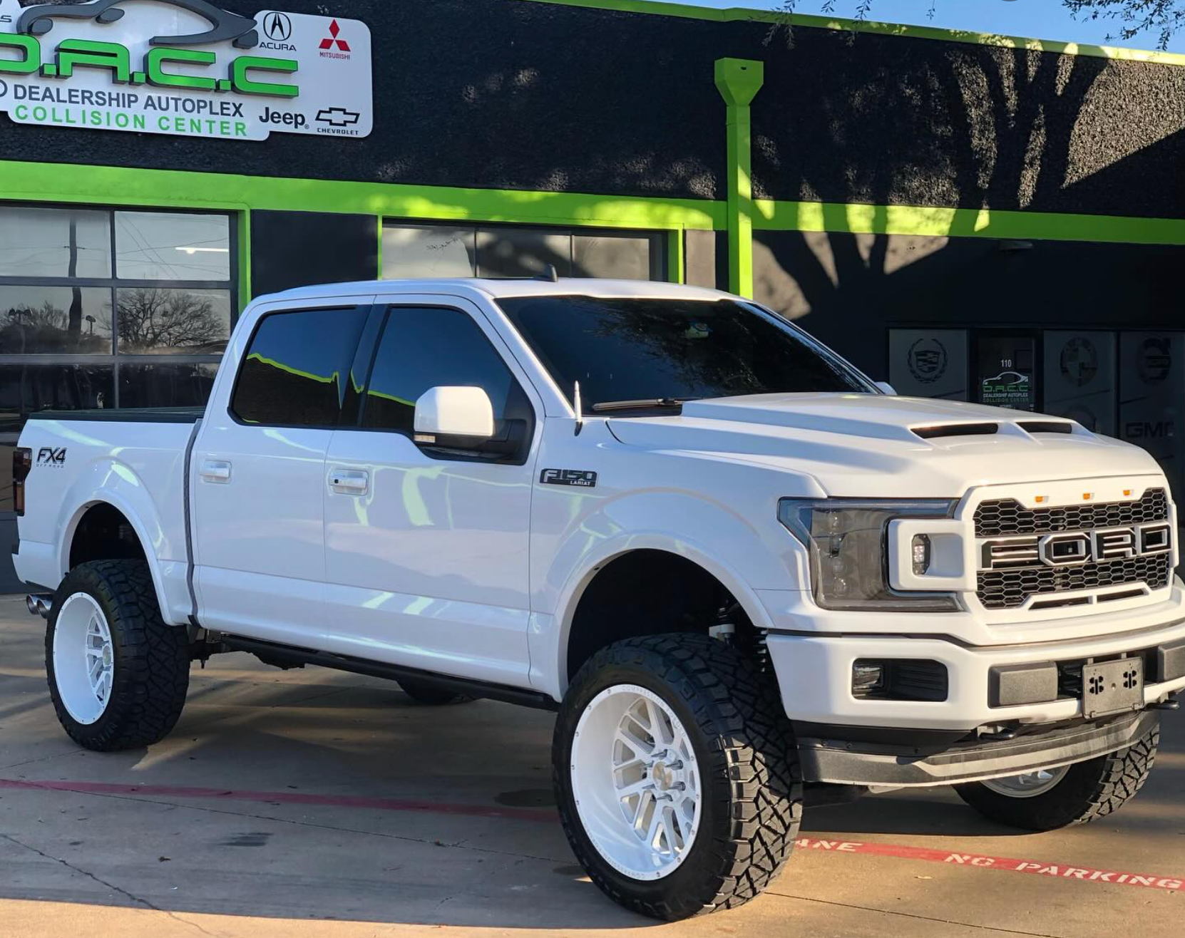 White Ford F-150 truck with large white rims and a raised suspension parked in front of an auto shop.