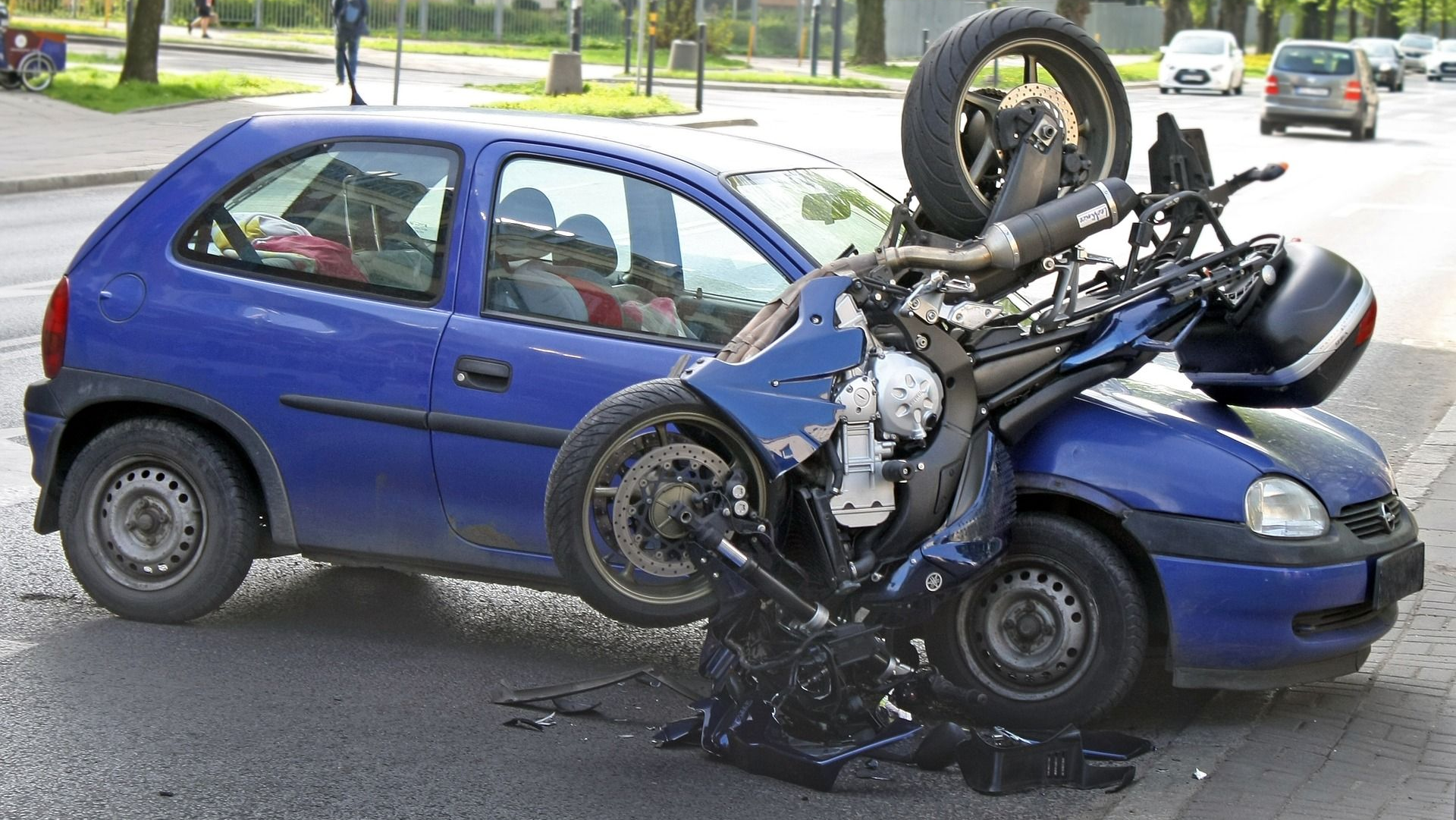 Blue car crashed with a motorcycle on a street; both vehicles damaged.
