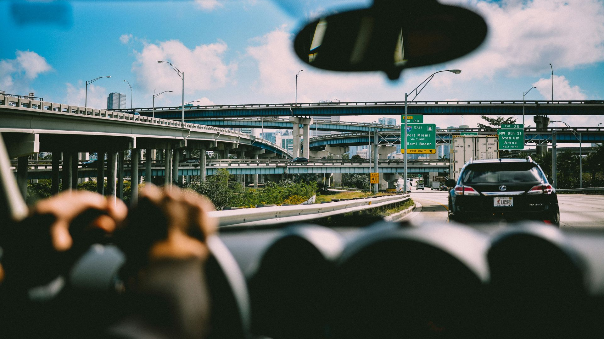 View from inside a car driving on a highway, with overhead bridges, a blue sky, and other vehicles.