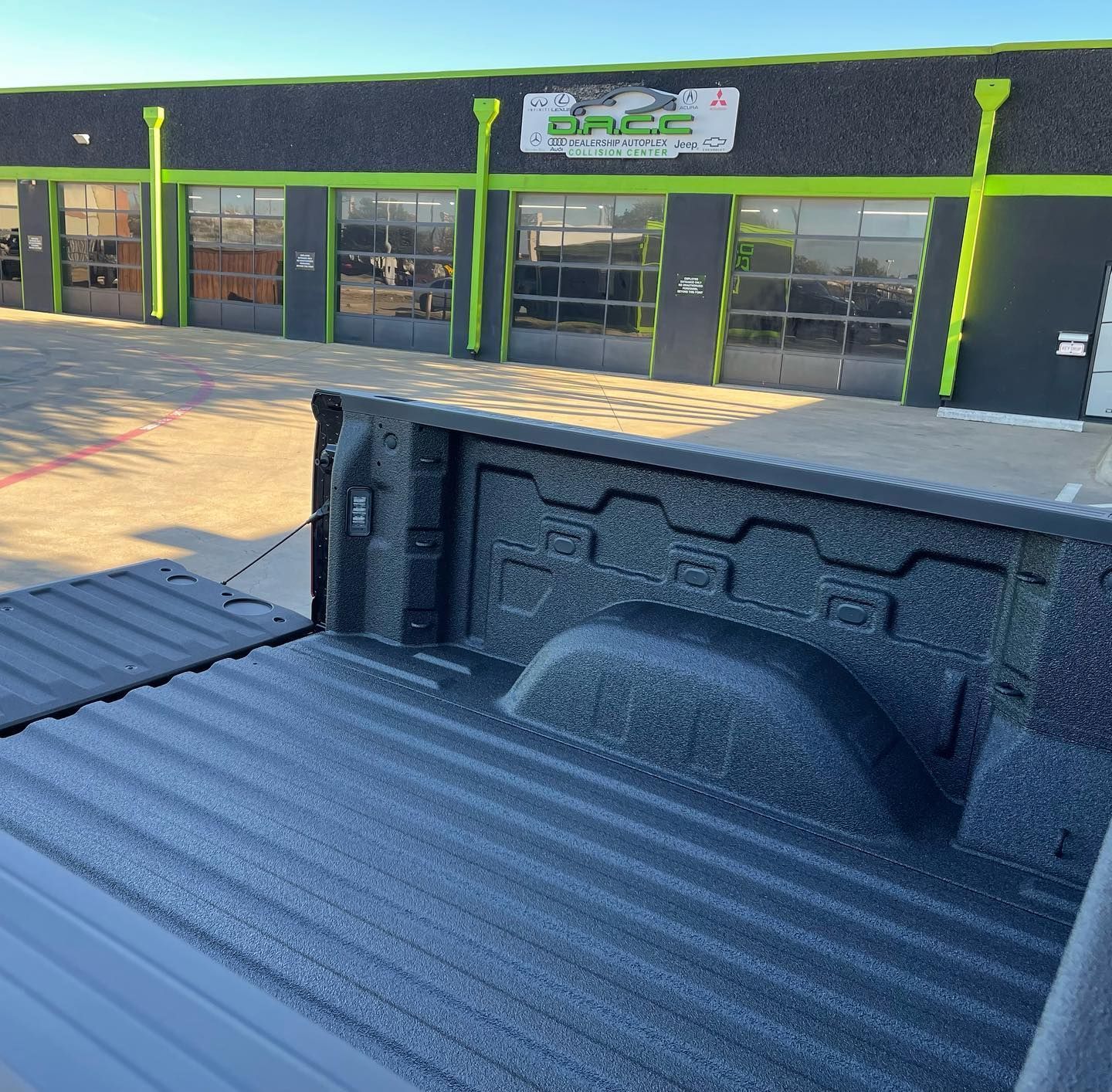 Truck bed with a textured coating in front of a gray building with green accents and garage doors.