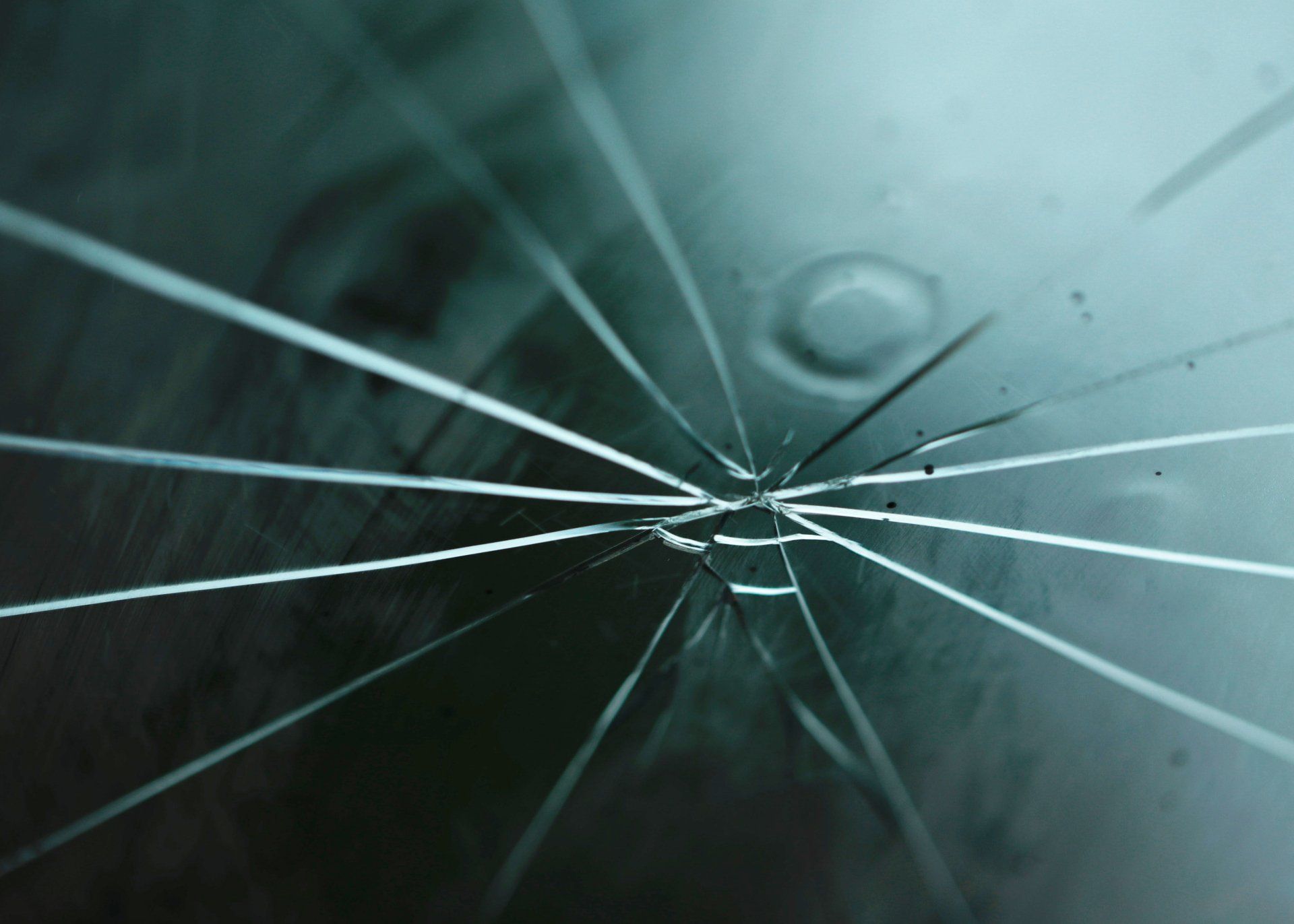 Cracked glass surface, radiating lines of fracture from a central point. Turquoise and dark teal tones.
