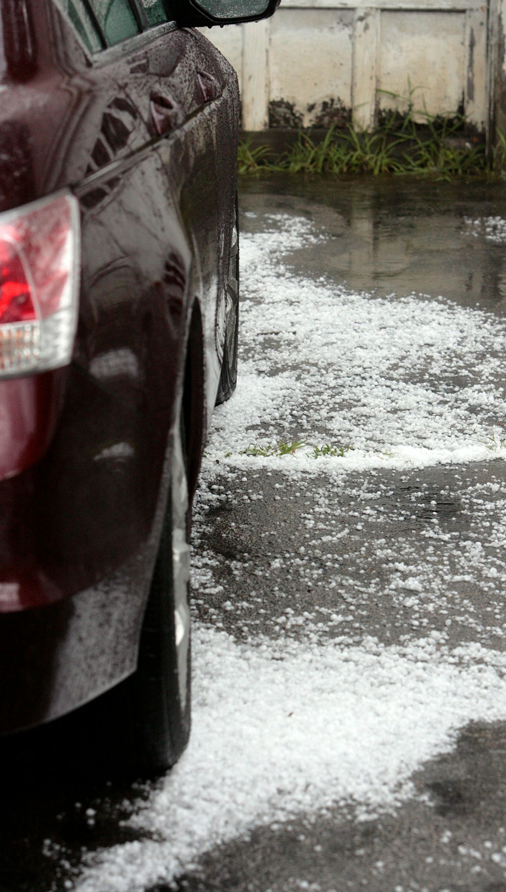 Maroon car parked on hailstones covering asphalt.