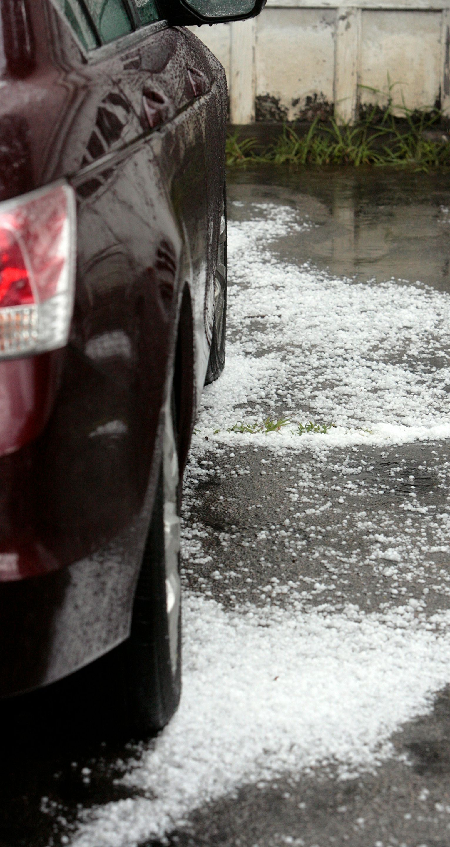 Maroon car parked on hailstones covering asphalt.