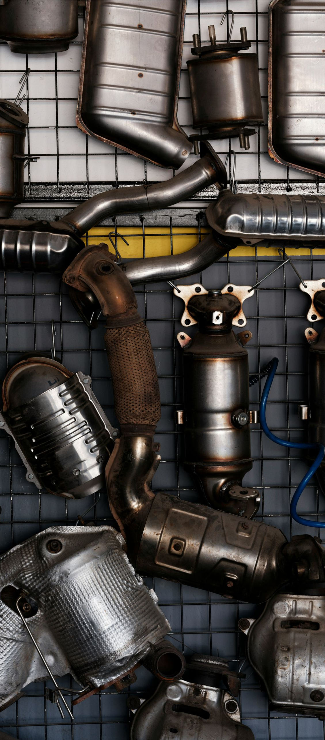 A large collection of metal automotive catalytic converters arranged on a wall-mounted wire grid.