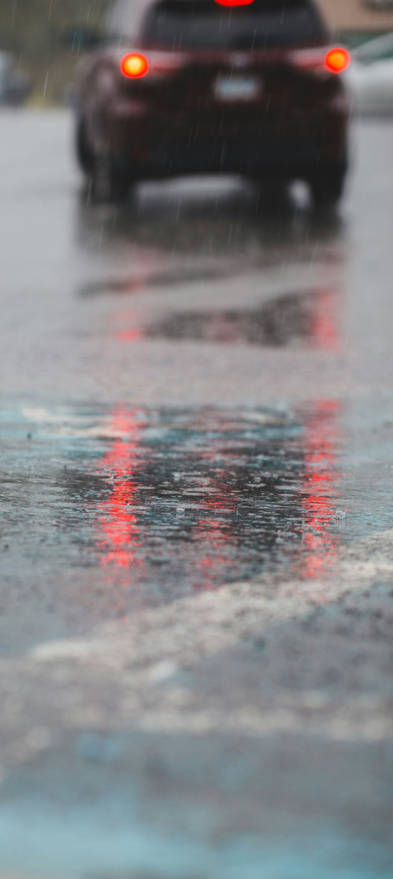 Rainy street scene with red taillights reflecting in a puddle; another car in the distance.