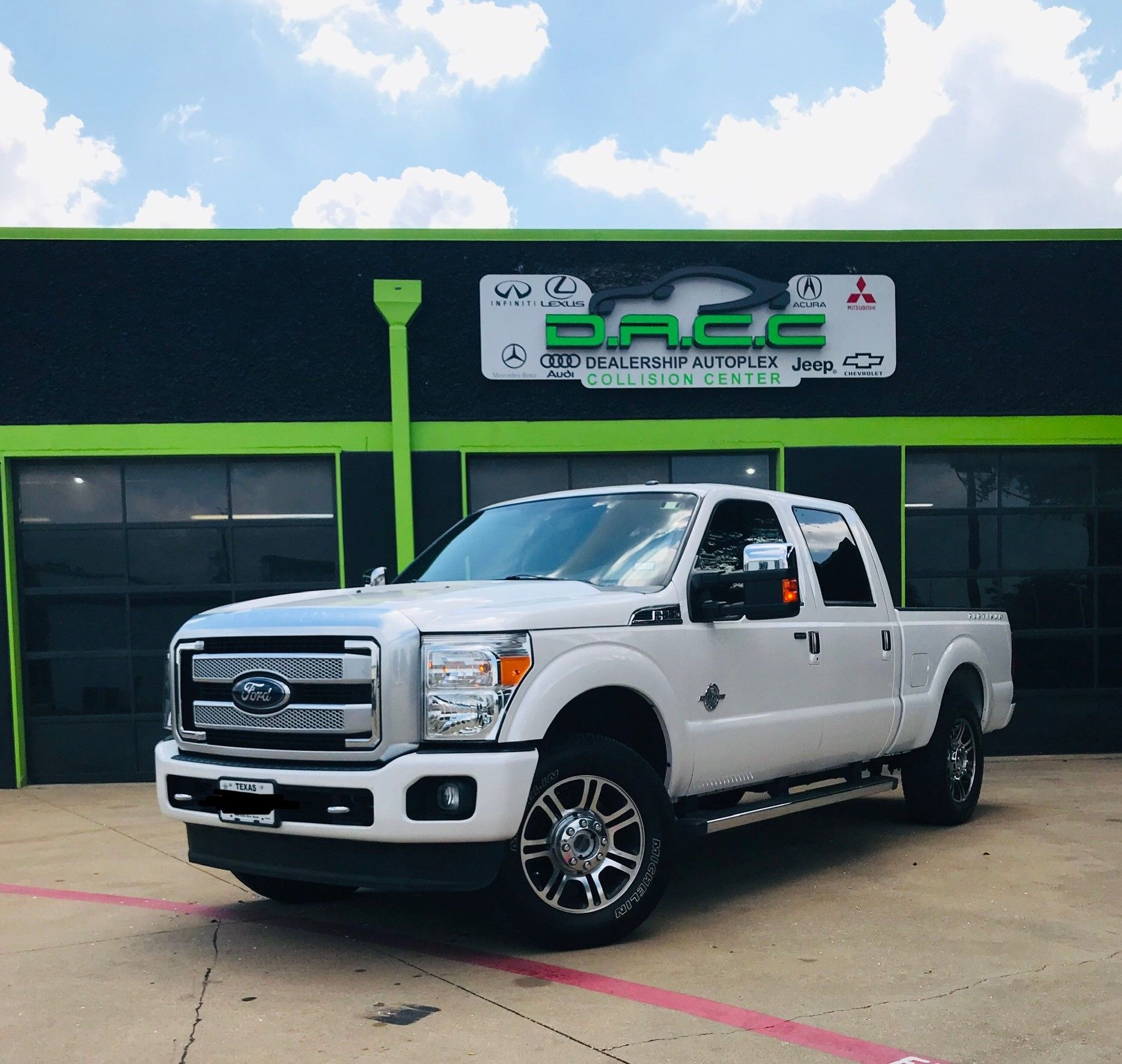 White Ford F-350 pickup truck parked in front of a green and black auto repair shop on a sunny day.