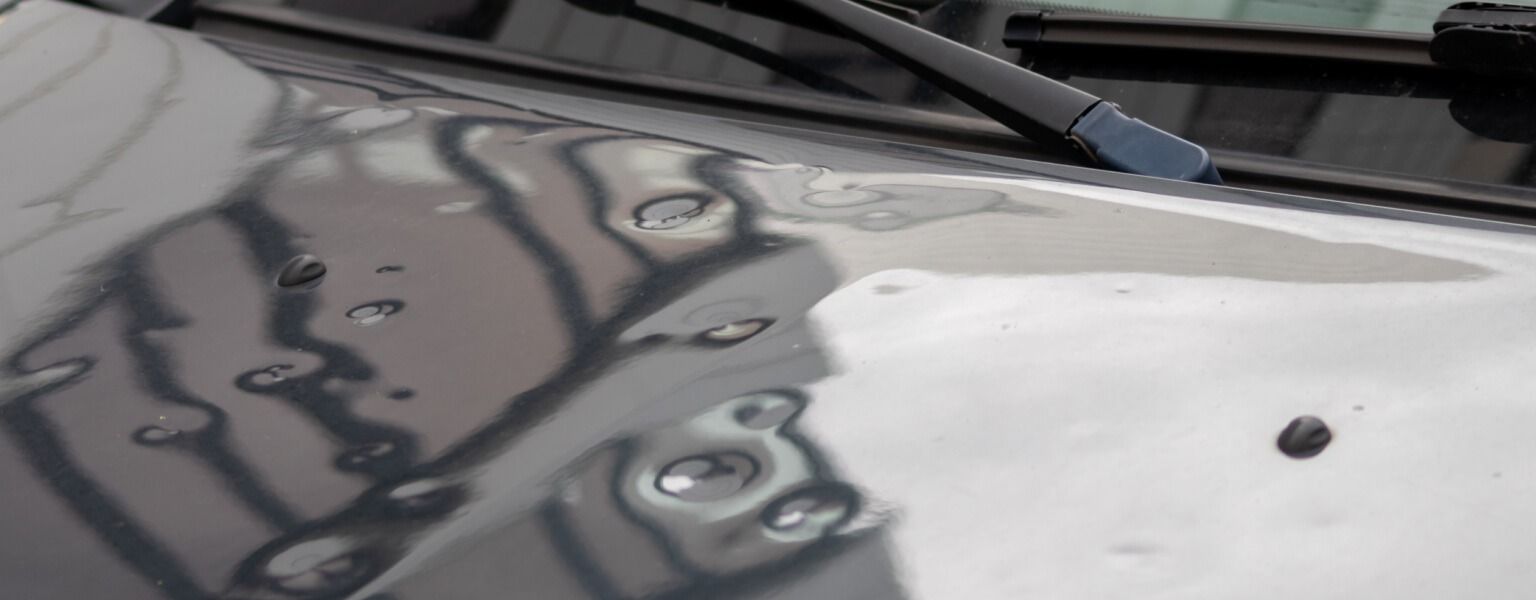 Car hood with water droplets, reflecting the sky and surroundings.