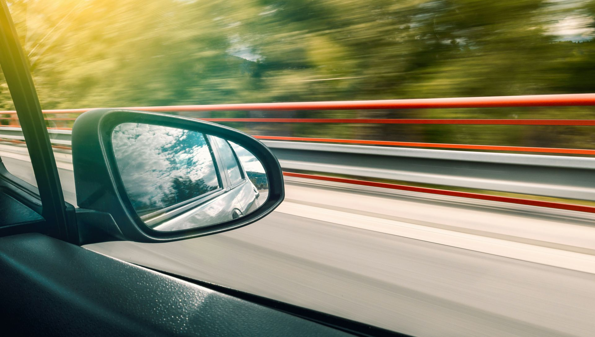 Car side mirror with highway view; blurred motion, sunny day.