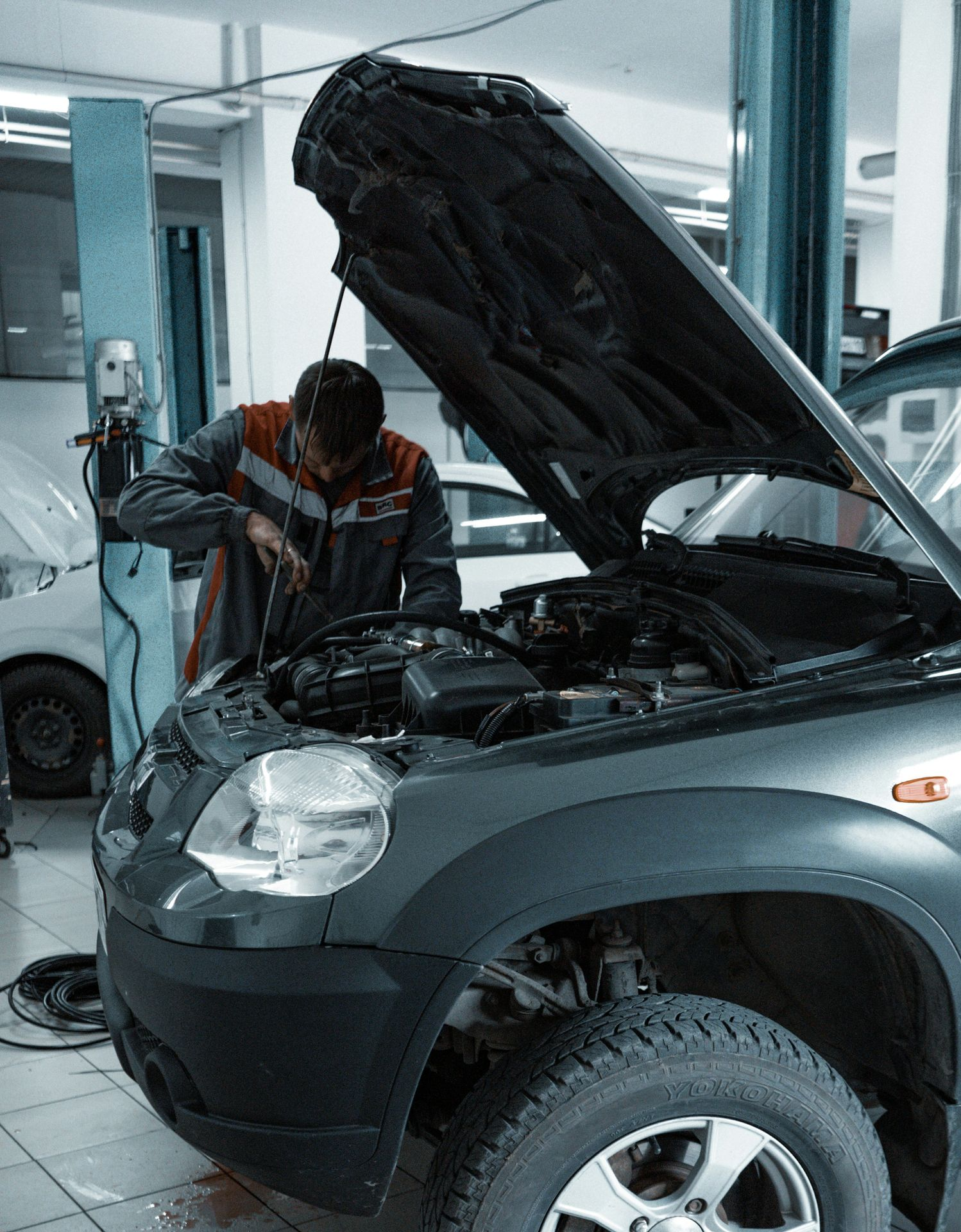 A mechanic works on the engine of a dark gray SUV with its hood open in a professional garage.