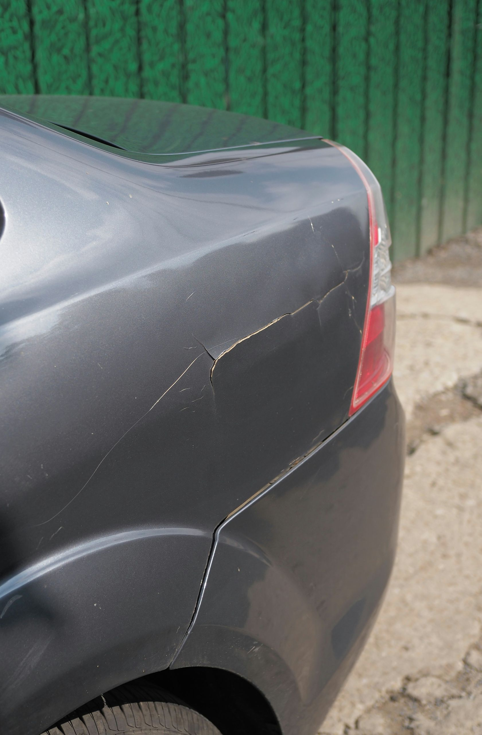 A close-up view of the rear quarter panel of a gray car showing deep scratches and paint damage near the tail light.