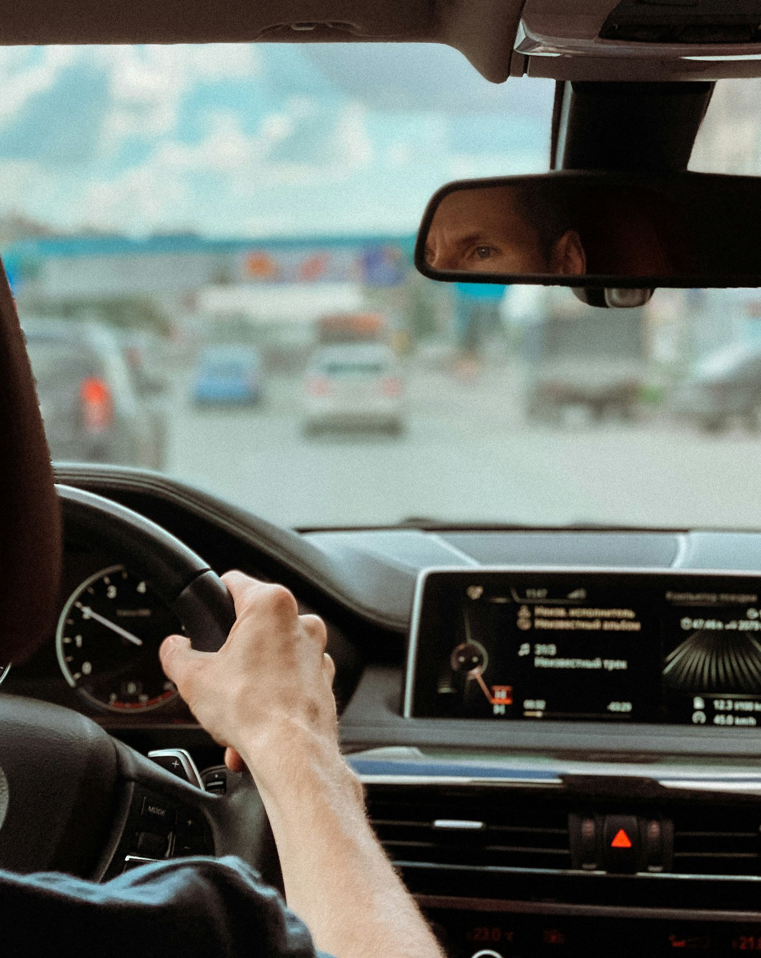 Person driving a BMW, holding the steering wheel. Traffic visible through windshield.