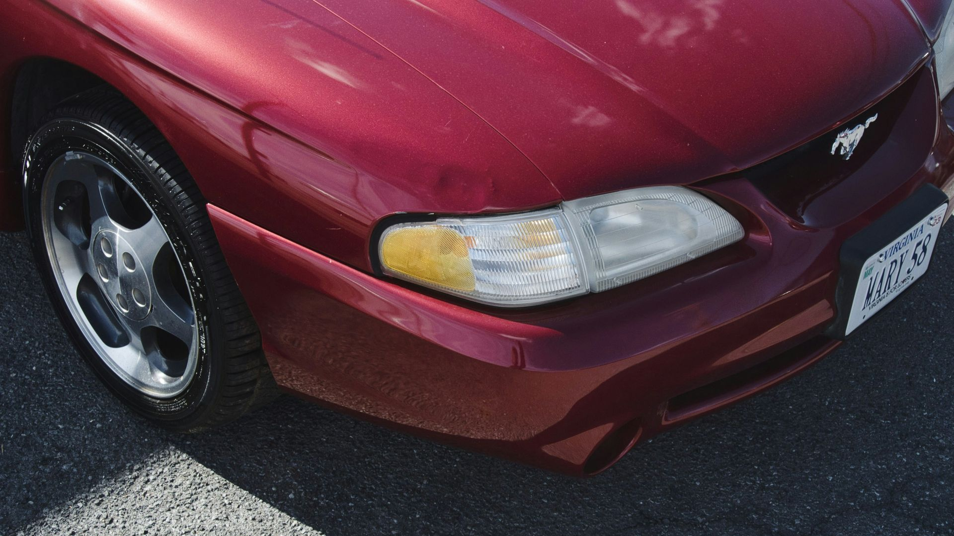 Red Ford Mustang front end with headlight and license plate.