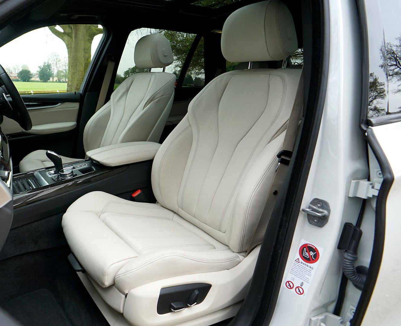 Beige leather car seats inside a white vehicle. The front seats are visible, featuring adjustable controls and a headrest.