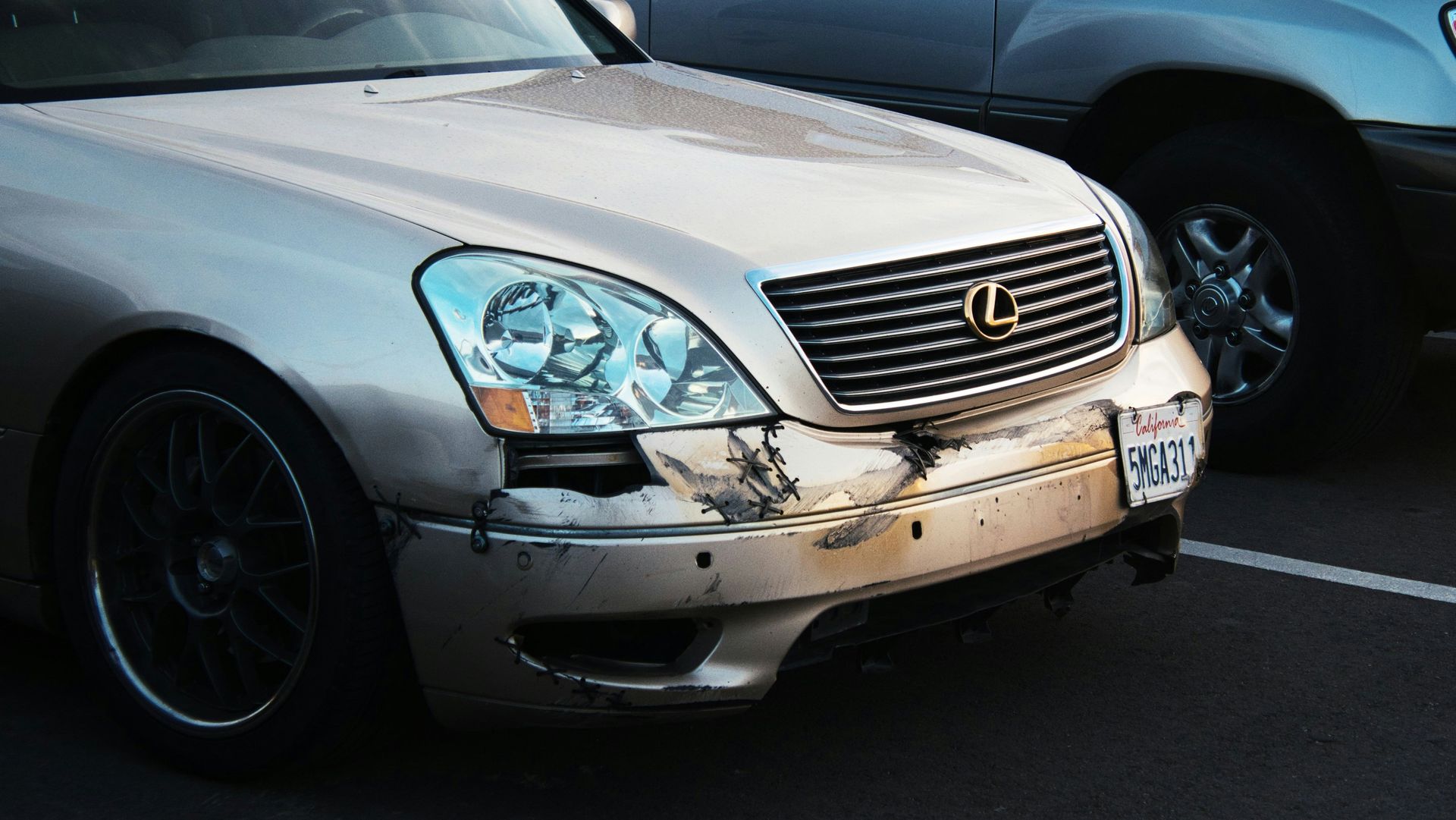 Damaged silver Lexus sedan with front-end collision damage in a parking lot