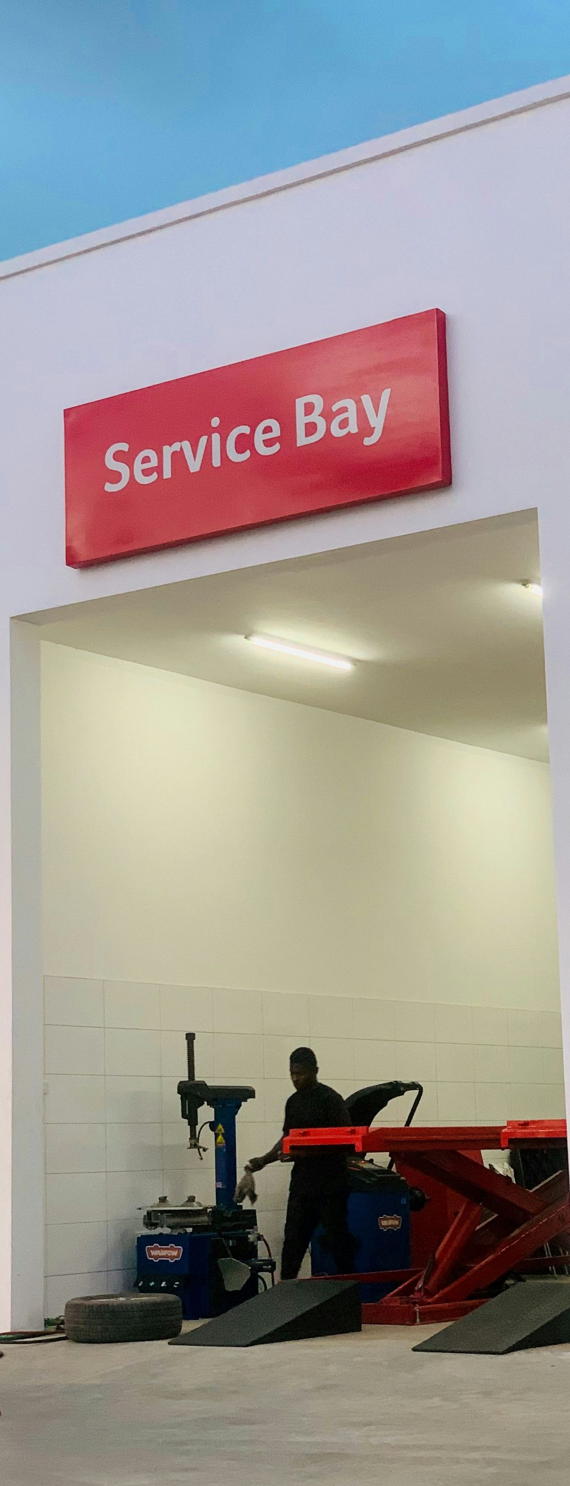 A service bay garage with a red sign and a technician operating tire changing equipment.