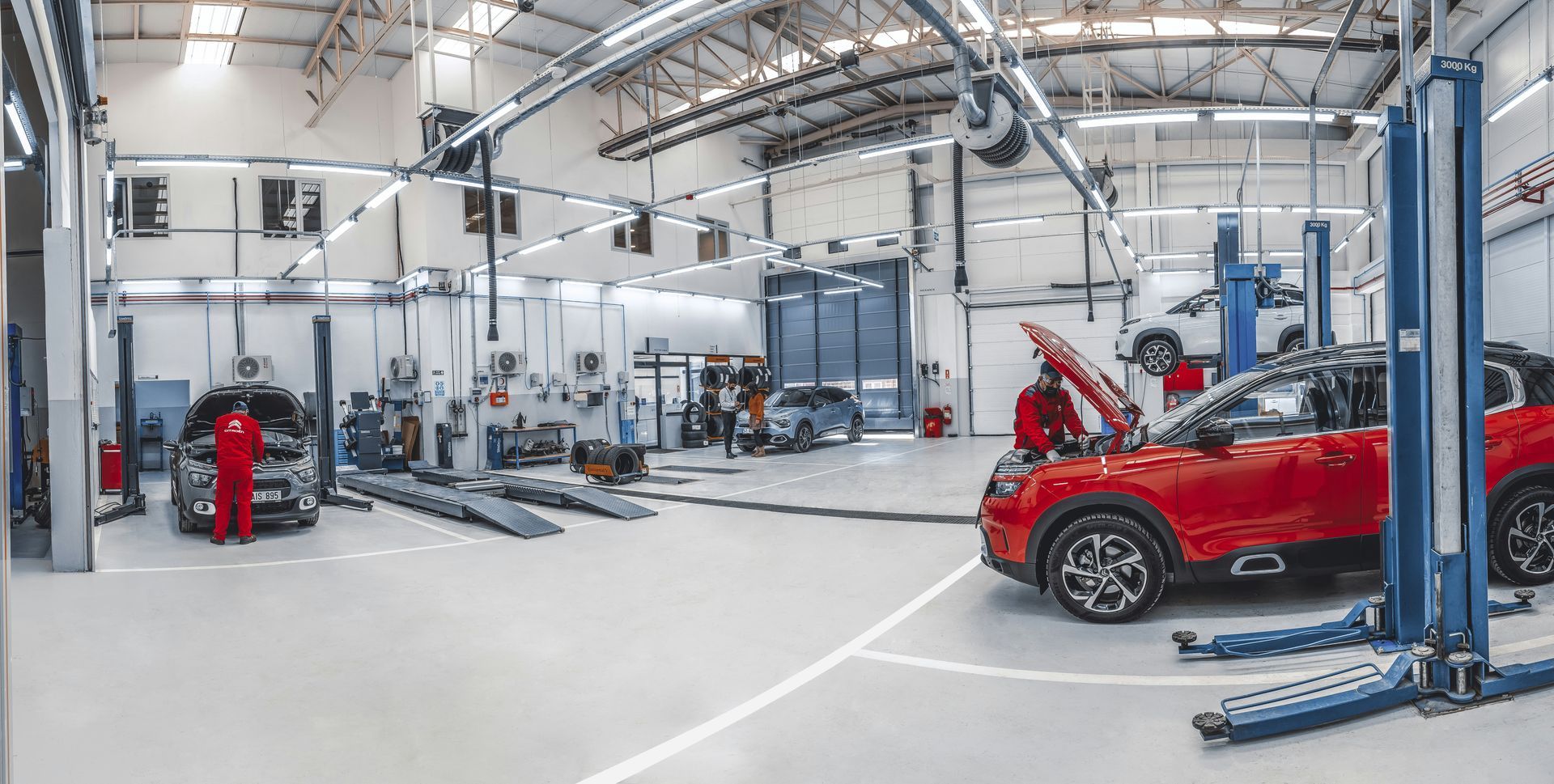 Mechanics work on vehicles in a bright, modern, and spacious automotive repair shop with multiple service bays.