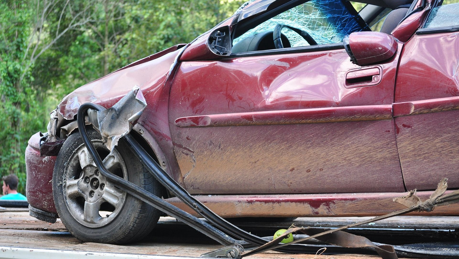 Damaged red car involved in a wreck, with smashed windshield and crumpled front end.