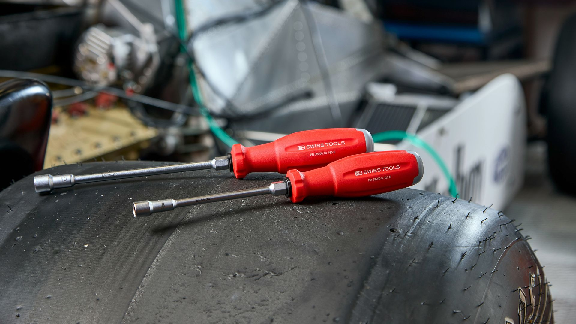 Two red-handled nut drivers resting on a large, wet racing kart tire in a workshop.