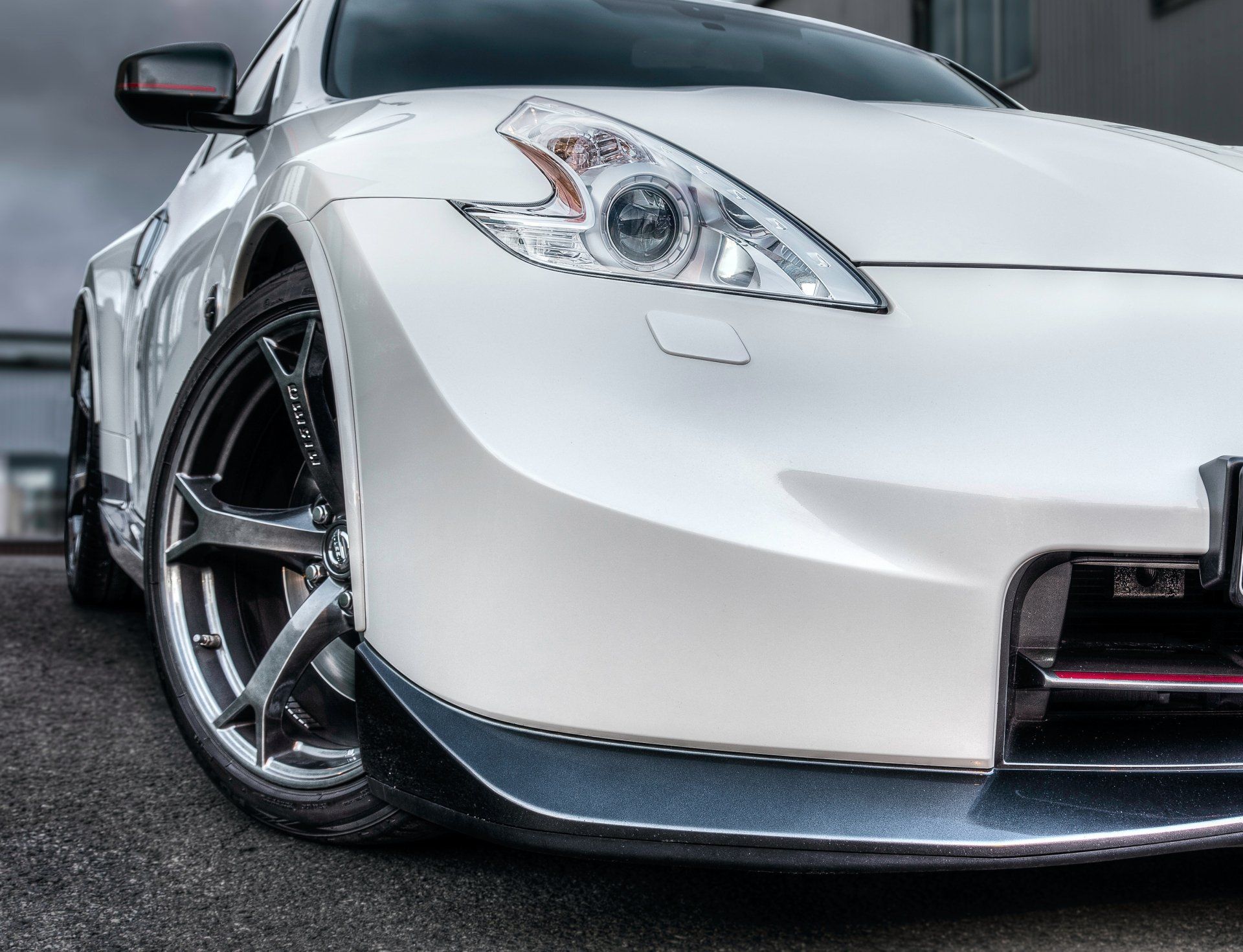 White sports car, low angle. Front view showing headlight, wheel, and front spoiler.