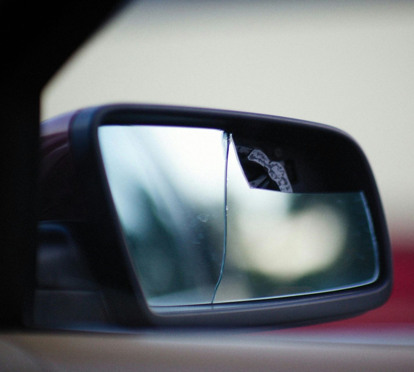 Broken car side mirror, reflecting blurry background, cracked glass.