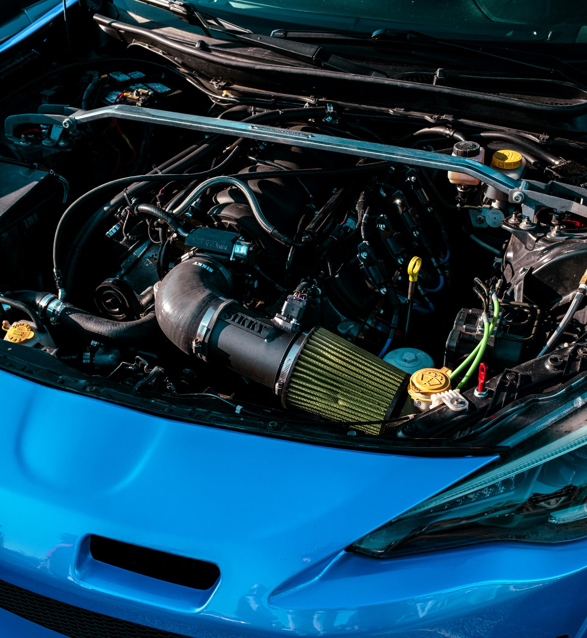 Blue car engine bay, open hood. Black engine parts with yellow air filter.