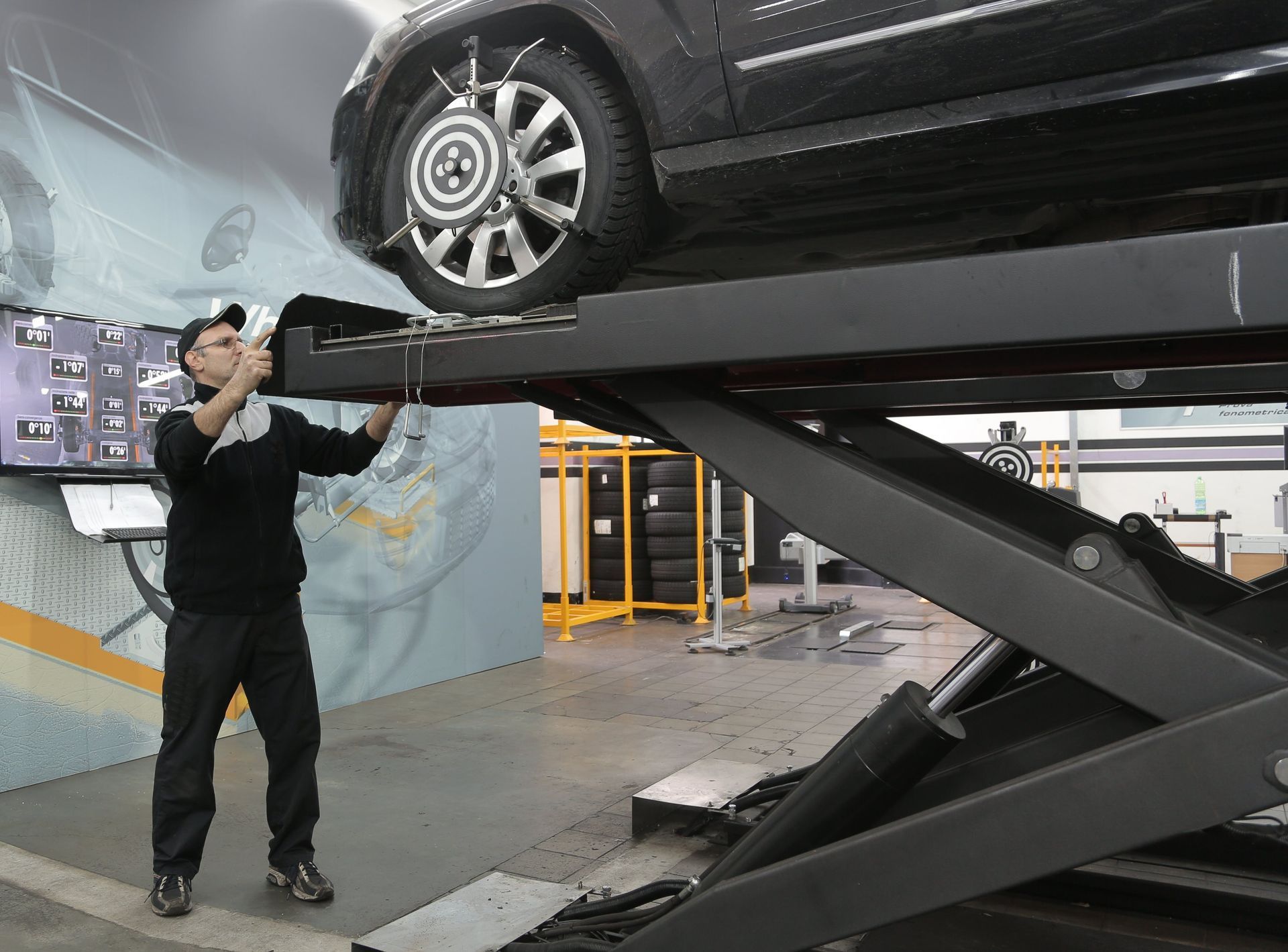 Mechanic adjusting equipment on a car lifted on a hydraulic lift. They are in a garage.