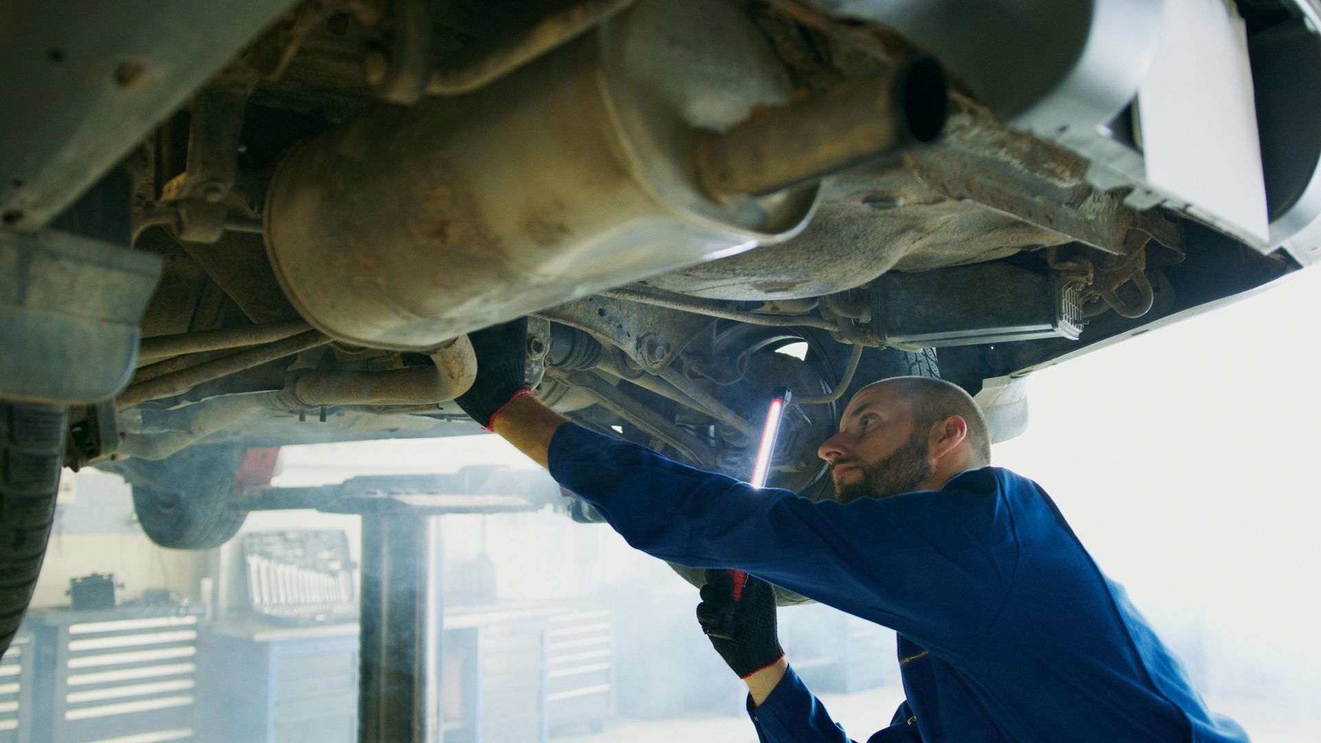 Mechanic using a power tool under a lifted car in a garage