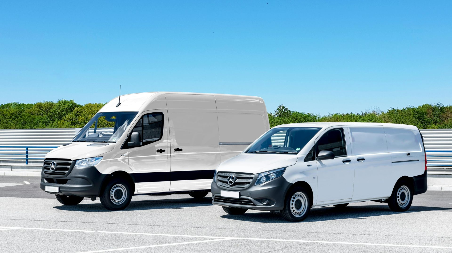 Two white cargo vans parked on a paved lot on a sunny day.